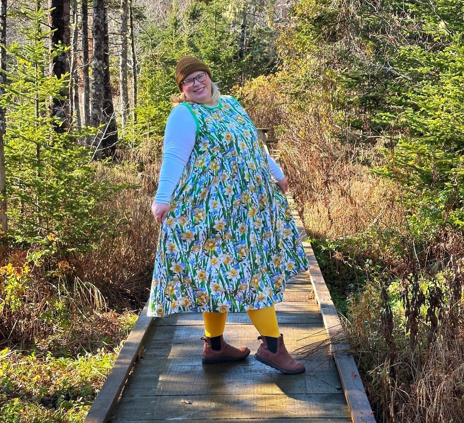 Person wearing a floral dress standing on a wooden path in a forest